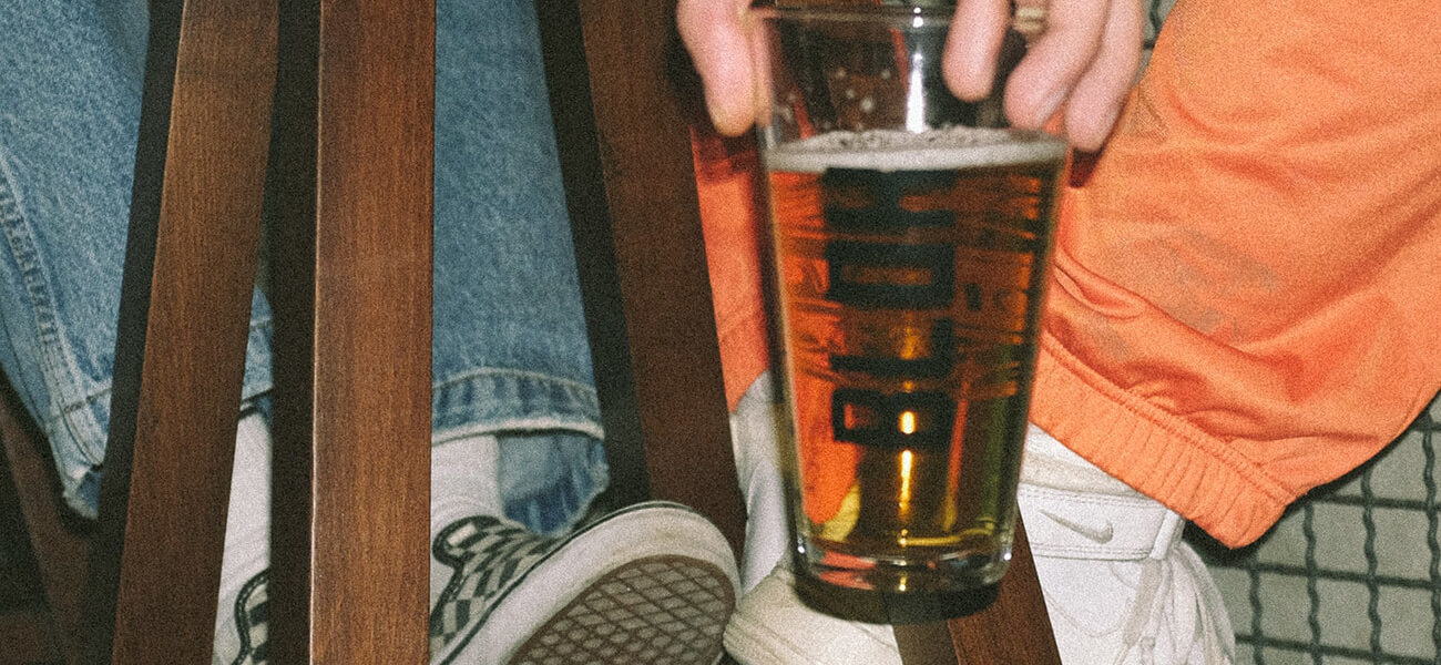 pint-glass-full-of-beer-held-low-next-to-sneakers-on-barstool-beer-chronicle-houston-best-beer-bars-to-visit-in-houston_0000_yasin-aribuga-daMT4OR3Eac-unsplash